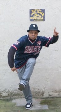 Photo de Richard Justin, professeur de danse hip hop à Marseille, dans un mouvement de pointing avec pour tenue un tee-shirt américain et un chapeau noir.